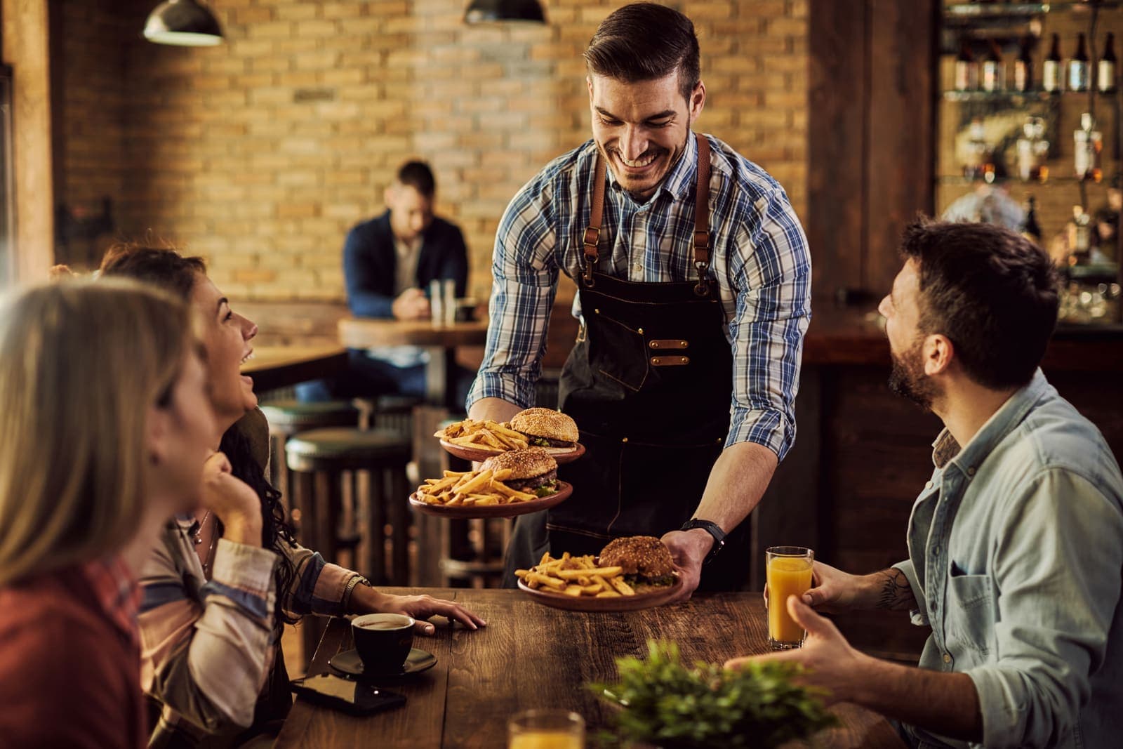 Garçom servindo hambúrgueres e batatas a um grupo de clientes em um bar